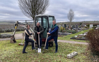 Aanke Renker und Andreas Hofreuter mit Spaten auf dem Harxheimer Friedhof vor einem kleinen Bagger